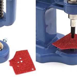 May include: Close-up of a blue press machine with a silver spring and black punch. A red, glittery piece of material is being punched. The machine is designed for crafting and creating custom designs.