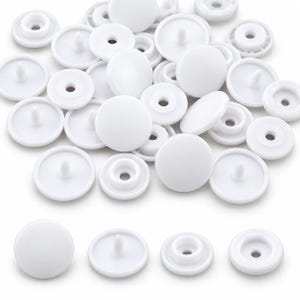 May include: A collection of white plastic snap fasteners, including both cap pieces with a central prong and socket pieces with a hollow center. These circular components are arranged in a pile, with four individual pieces displayed in a row below.