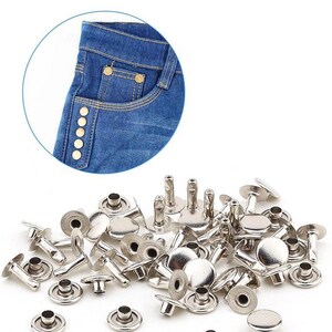 Peut inclure: Un ensemble de rivets métalliques argentés, avec un gros plan sur un jean bleu orné de boutons dorés. Les rivets ont une tête plate et circulaire et une tige pour les fixer au tissu. Idéal pour les projets de couture.