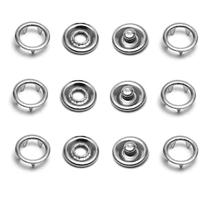May include: A collection of twelve silver-colored snap fasteners. Each fastener consists of two parts: a circular ring with three prongs and a circular snap with a central stud. The fasteners are arranged in a grid pattern against a white background.