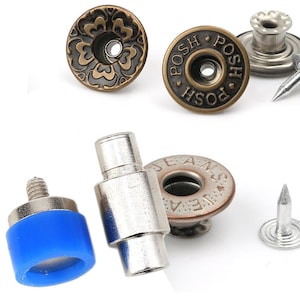 May include: Close-up of various metal jean button and rivet hardware. Includes antique brass and silver-toned buttons with decorative designs and the word "POSH". Also shown are rivets and a blue rubber-based tool.