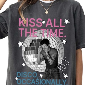 Op de afbeelding: Een antracietgrijs t-shirt met een grafische print van een discobal en een persoon die een bril rechtzet. De tekst luidt KISS ALL THE TIME. DISCO, OCCASIONALLY. Het ontwerp bevat witte sterren en een handtekening in wit schrift aan de rechterkant.