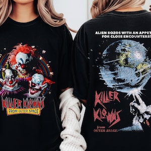 May include: A black t-shirt featuring a graphic of three clowns with red hair and makeup, with the text "KILLER KLOWNS FROM OUTER SPACE" below. The back shows a planet graphic with the text "ALIEN BOZOS WITH AN APPETITE FOR CLOSE ENCOUNTERS!"