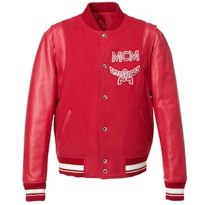 Pode incluir: Casaco universitário vermelho com mangas de couro. O casaco apresenta um patch branco com o logotipo MCM no peito e listras brancas nos punhos e na bainha. Possui fecho de botões e gola canelada.