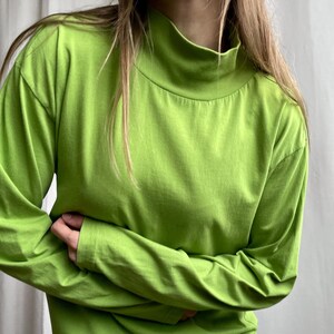 May include: A long-sleeved, lime green turtleneck shirt. The shirt is made of a soft fabric and has a high neckline. The sleeves are long and cover the arms. The shirt is a solid color and has a simple design.