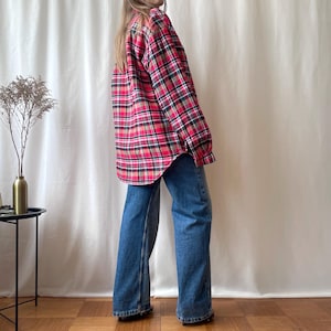 Pode incluir: Uma camisa de flanela xadrez vermelha e preta com mangas compridas e fecho de botões. A camisa é combinada com jeans azuis. O traje é casual e confortável.