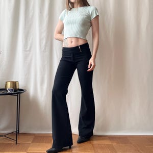 May include: Black flared trousers with a zip fastening, worn with a light green ribbed crop top. The trousers are high-waisted with a wide leg. The top has short sleeves. The outfit is displayed on a person.