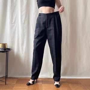 May include: Black and green plaid trousers with a high waist and pleated front. The pants are worn with black and white heels. The fabric has a subtle sheen. The trousers are a classic style.