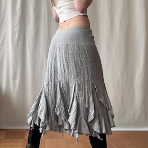 May include: A light gray midi skirt with a textured fabric and a flared, ruffled hem. The skirt has a high waist and a flowing silhouette, suitable for casual or semi-formal wear. The skirt is made of a lightweight material.