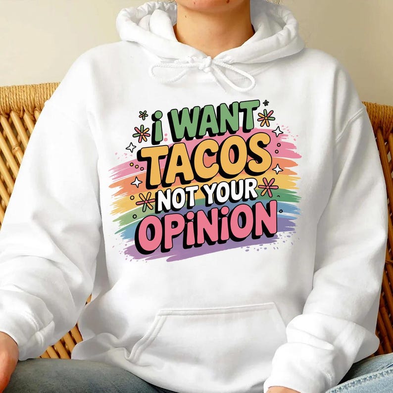 May include: White hooded sweatshirt with the text "I WANT TACOS NOT YOUR OPINION" in colorful, playful lettering. The design includes a rainbow-colored background and decorative stars and flowers.