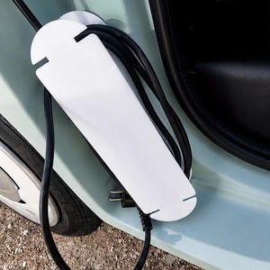May include: A white charging cable holder with a black charging cable and plug. The holder is mounted on a light blue car. The cable is plugged into the car.