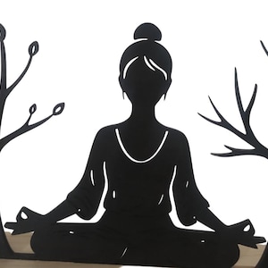 May include: Black metal silhouette of a person in a yoga pose, seated with legs crossed and hands in a meditative gesture. Two stylized trees flank the figure. The piece is mounted on a light-coloured wooden base, creating a serene, minimalist aesthetic.