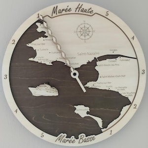 Puede incluir: Reloj de pared de madera con diseño de mapa. La esfera del reloj presenta un mapa marrón oscuro de una región costera, con nombres de lugares y una rosa de los vientos. Las manecillas del reloj son blancas y los números están alrededor del borde. Las palabras "Marée Haute" y "Marée Basse" están escritas en el reloj.