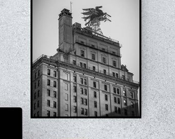 May include: Black and white photograph of a tall building with a unique metal structure on the roof. The building has many windows and is made of brick.