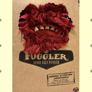 May include: A red, furry Fuggler toy with large white teeth and black eyes. The toy is on a cardboard backing with the words "Fugglers Funny Ugly Monster" and a warning label.