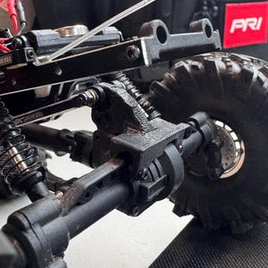May include: Close-up of a black RC car chassis with a focus on the suspension and wheel assembly. The image highlights the intricate details of the vehicle's components, including the shocks, axles, and tires. The text "PRI" is visible.