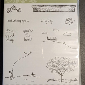 May include: A set of 10 rubber stamps with images and phrases related to home and family. The stamps include a house, a tree, a bench, a kite, a dog, flowers, and the phrases "Happy Home", "missing you", "enjoy", "it's a good day", and "you're the best!"