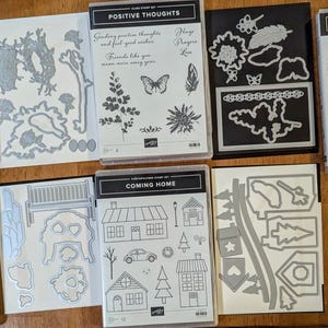 May include: A set of ten die-cut metal stencils for crafting. The stencils feature various designs, including flowers, birds, houses, and a bench. The stencils are in a variety of sizes and shapes. The stencils are made of silver metal and have a shiny finish.