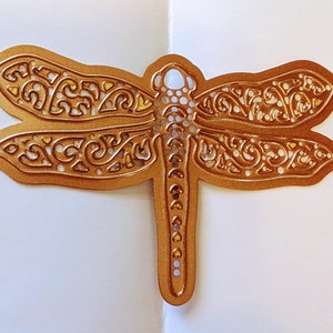 May include: A copper-colored dragonfly die cut with intricate details and a gold glitter finish. The dragonfly has a delicate, filigree design and is perfect for crafting projects.