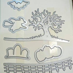May include: A collection of silver-colored metal die cuts in various Halloween-themed shapes. Includes a bat, witch on a broom, bare tree, clouds, pumpkin, and a fence. Ideal for crafting projects.