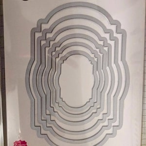 May include: A set of six metal dies for crafting. The dies are shaped like ornate frames with rounded corners. The dies are designed to be used with a die-cutting machine. The package includes instructions for use.  6 Dies • 6 Poinçons • 6 Troqueles Framelits™