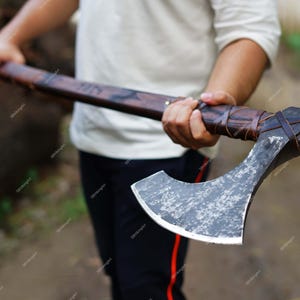 May include: A handcrafted axe with a dark wooden handle and a weathered, silver-colored blade. The handle is wrapped with brown leather for grip. The axe appears to be a historical or Viking-style design.