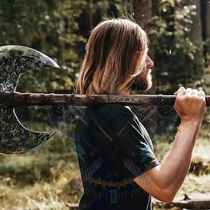 May include: A large, double-bladed axe with a textured, silver-colored head and a wooden handle. The handle is wrapped with red leather near the grip. The axe is being carried over the shoulder.