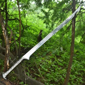 May include: A silver sword with a curved blade and ornate handle. The blade has a textured pattern, and the handle features decorative carvings. The sword is set against a backdrop of green foliage and tree branches.