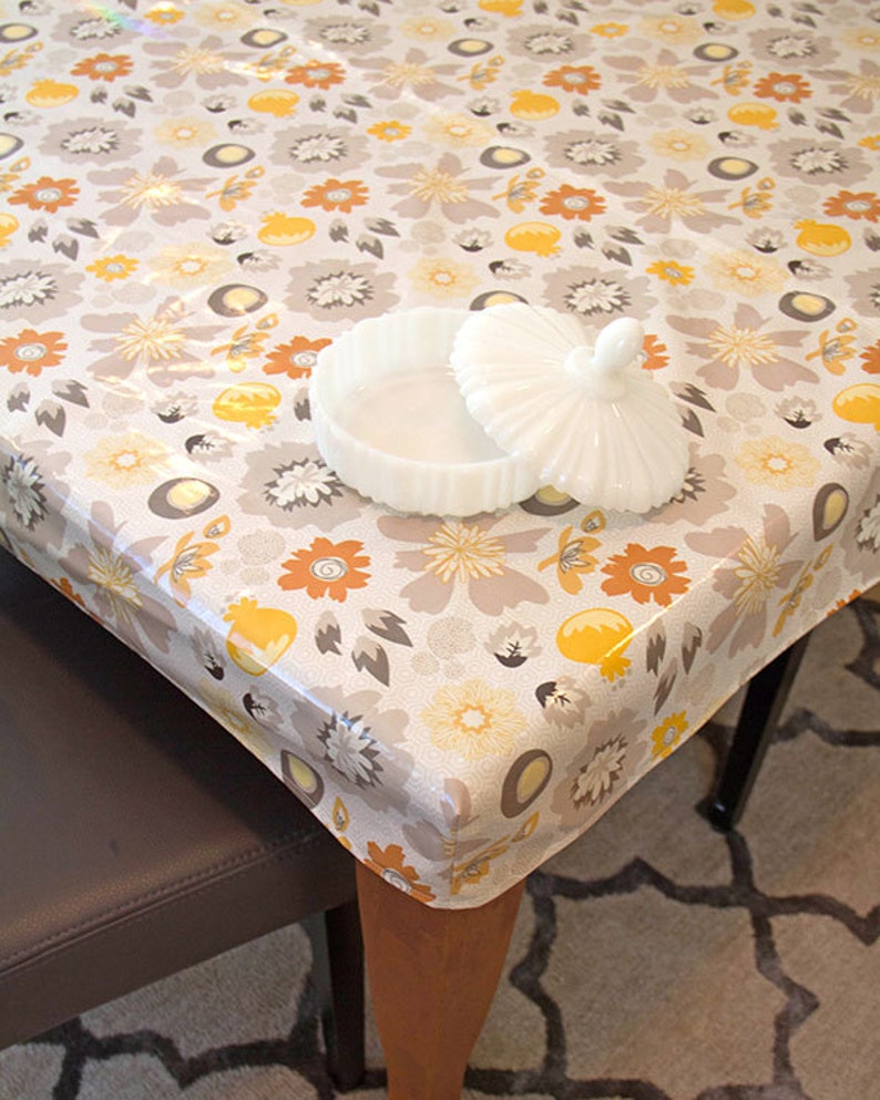 Puede incluir: Un mantel de mesa blanco con flores con un patr&oacute;n floral amarillo y naranja. Un plato de cer&aacute;mica blanco con tapa est&aacute; sobre el mantel.