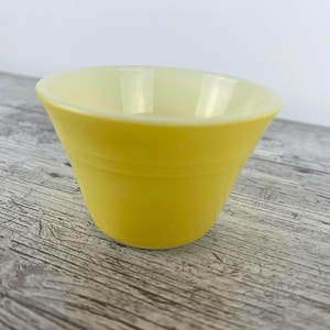 May include: A vibrant yellow bowl with a gently sloping design. The bowl has a smooth, shiny surface and a pale yellow interior. It rests on a weathered, grey wooden surface. This bowl is suitable for serving food.