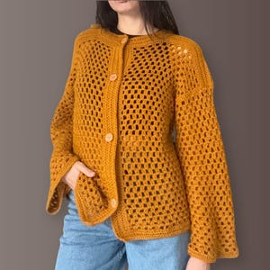 May include: Mustard yellow crochet cardigan with a button-up front and flared sleeves. The open weave design creates a breathable, lightweight feel. The cardigan features three wooden buttons and a relaxed fit, perfect for layering.