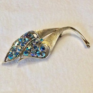May include: A silver tone brooch with a leaf design and blue iridescent rhinestones.