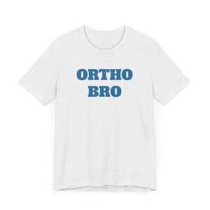 May include: A light grey t-shirt featuring the blue text "ORTHO BRO" across the chest. The shirt has a crew neck and short sleeves, suitable for casual wear.