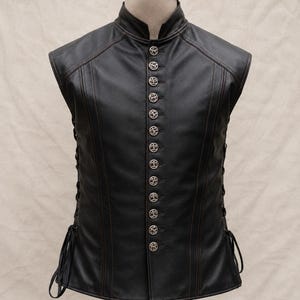 May include: Black leather vest with a high collar and decorative silver buttons. The vest has a tailored fit, with side lacing detail. The stitching is a contrasting brown colour. This vest is a stylish addition to any wardrobe.
