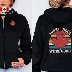 May include: Black zip-up hoodie with a red maple leaf emblem. The back of the hoodie displays a retro design with a red maple leaf and the text "SORRY. NOPE. WE'RE GOOD."