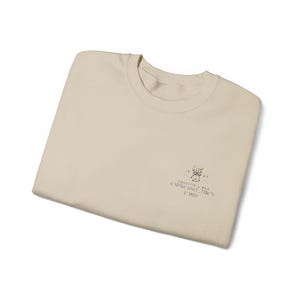 Könnte beinhalten: Ein gefaltetes, cremefarbenes Sweatshirt mit Rundhalsausschnitt. Das Sweatshirt hat eine kleine Grafik und den Text "ROSETTE & RUE ESPRESSO THEN PARIS". Die Grafik ist eine Zeichnung einer Kaffeetasse.