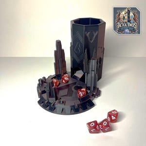 Könnte beinhalten: Ein 3D-gedruckter Würfelturm in Form einer futuristischen Stadt mit einem Schwarz-Grau-Farbschema. Der Turm hat eine sechseckige Basis und ein abnehmbares Oberteil. Es gibt sechs rote Würfel mit weißen Zahlen auf der Basis des Turms und verstreut um ihn herum. Der Turm ist mit "Tactical Towers 3D Print Shop" beschriftet.