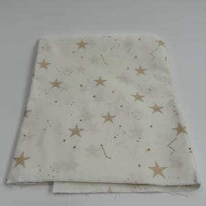 May include: White fabric with a gold star pattern. The stars are of varying sizes and are scattered randomly across the fabric.