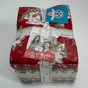 May include: A stack of red, white, and green fabric squares with a floral print. The fabric is wrapped in plastic and tied with a ribbon. The fabric is labeled "Stitch with Love" and "A1 Bonn Fabrics".