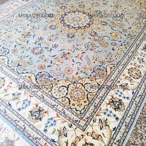 May include: A large, light blue rug with an intricate floral pattern and a cream-colored border. The rug features a central medallion design and is adorned with various floral motifs in shades of beige, pink, and blue. The text "MSRAGSLOOM" is visible on the rug.