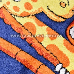 May include: A close-up of a colorful rug featuring a giraffe design. The rug has a blue background with orange and yellow giraffe details. The text "MSRAGSLOOM" is visible on the rug.