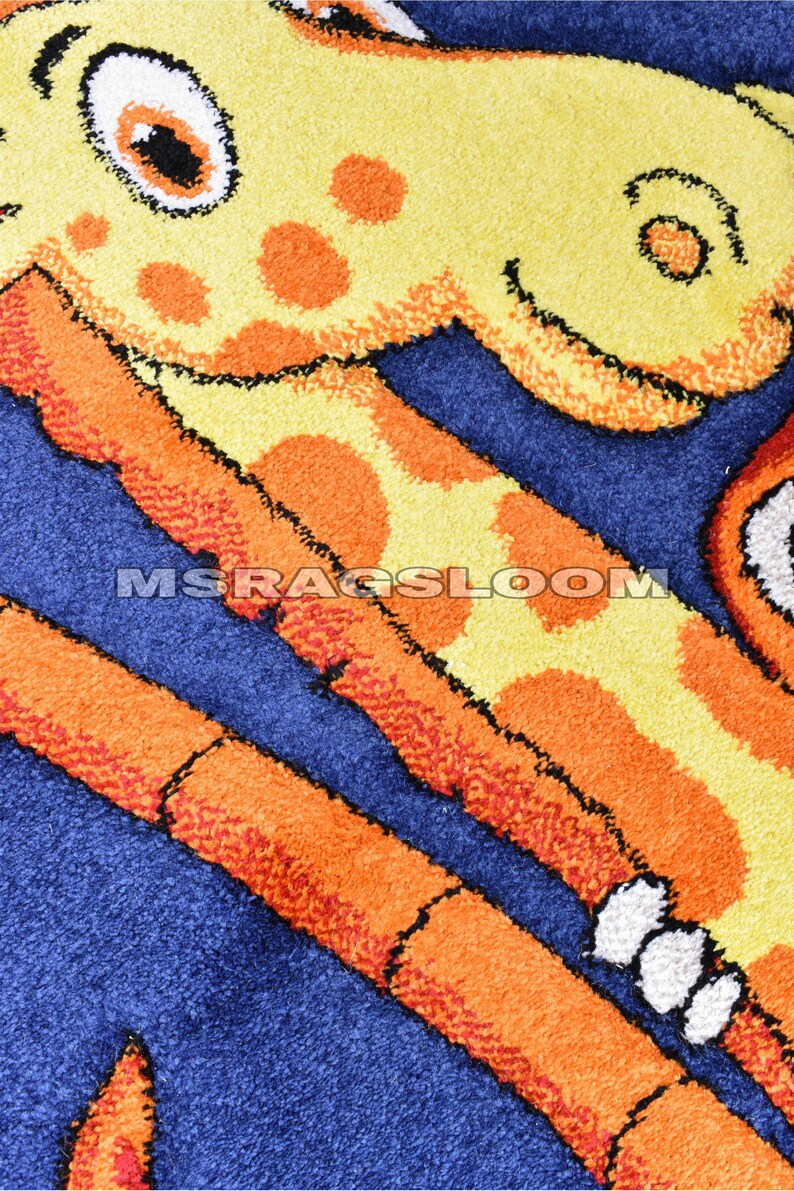 May include: A close-up of a colorful rug featuring a giraffe design. The rug has a blue background with orange and yellow giraffe details. The text "MSRAGSLOOM" is visible on the rug.