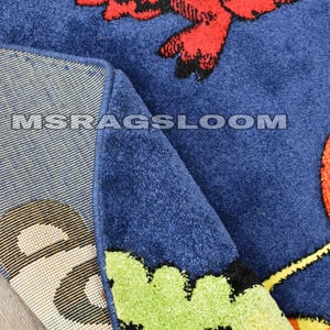 May include: Blue area rug with a colorful bird design. The rug features a large red bird with black accents and a yellow beak. The rug's edge is a darker blue, and the text "MSRAGSLOOM" is visible.