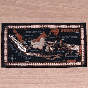 May include: A rectangular black textile featuring a map of Indonesia with surrounding seas and the word "Indonesia" in orange. The map is detailed with brown and white accents, and the border has a decorative pattern.