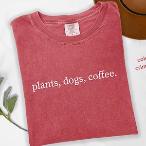 May include: Crimson red t-shirt with the text "plants, dogs, coffee." printed in white.