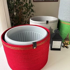 May include: A bright red woven rope basket with a gold-toned thread accent and a black leather tab featuring a gold rivet. Inside sits a light gray plastic planter with a ribbed interior. A black lantern with the text SNY is nearby.