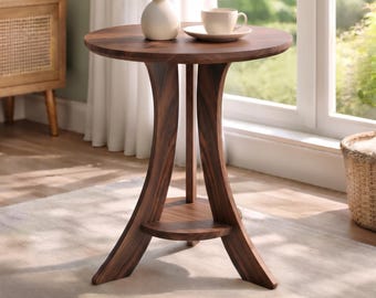 Può includere: Un tavolino rotondo in legno scuro con tre gambe curve e un ripiano circolare inferiore. Sul piano del tavolo si trovano un vaso in ceramica bianca con piccoli fiori bianchi e una tazzina in ceramica bianca su un piattino. Un badge circolare dorato riporta la scritta DIGITAL DOWNLOAD.