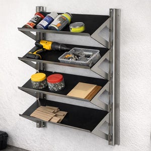 May include: A wall-mounted metal storage unit featuring four angled shelves with black surfaces. The shelves hold various items including spray cans, a yellow and black power drill, a clear plastic hardware bin, jars, and wooden blocks.