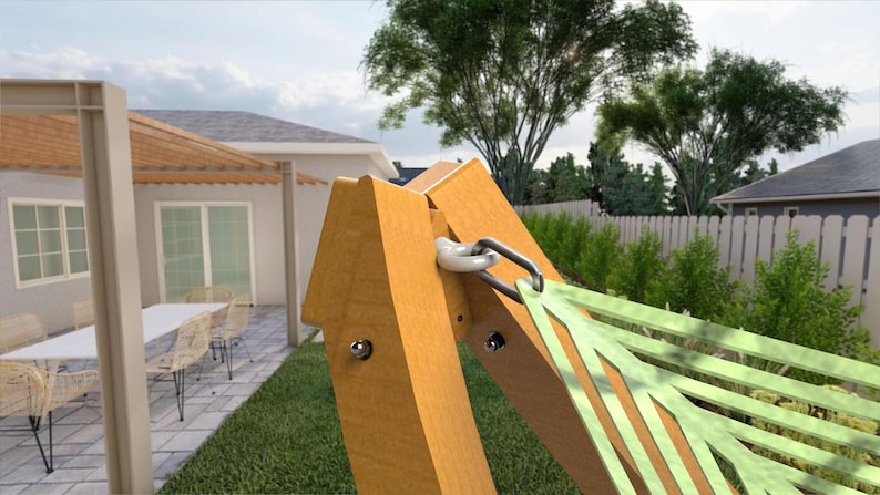 May include: A wooden hammock frame with a light green hammock. The frame is made of light brown wood and has a metal hook for the hammock. The background shows a house, patio, and green lawn.