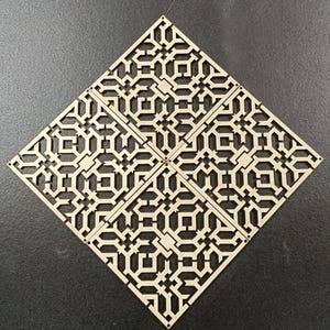 Puede incluir: Cuatro paneles de madera cortados con láser dispuestos en forma de rombo. Cada panel presenta un patrón geométrico repetitivo de cuadrados y rectángulos. Los paneles son de color beige claro sobre un fondo gris oscuro.